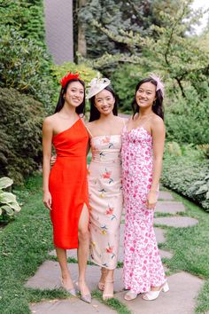 three young women standing next to each other in front of trees and flowers on the grass