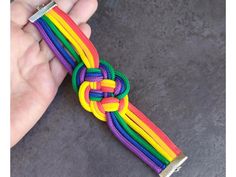 a hand holding a multicolored tie - knot on a gray surface with flowers in the background