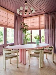 a dining room table and chairs with pink curtains on the window sill behind them