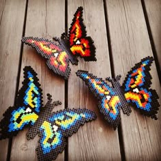 four colorful butterflies are sitting on a wooden surface, one is made out of perler beads