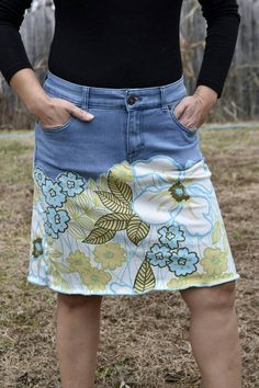 a woman wearing a skirt with flowers on it and her hands behind her back, standing in a field