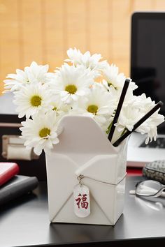 a vase with white flowers in it sitting on a desk next to a laptop computer