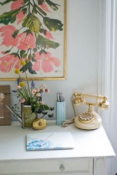 a white desk topped with a phone next to a vase filled with flowers and other office supplies