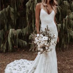 a woman in a white wedding dress holding a bridal bouquet and looking at the camera