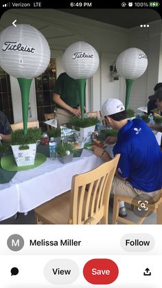 people are sitting at a table with plants and paper lanterns in the shape of golf balls