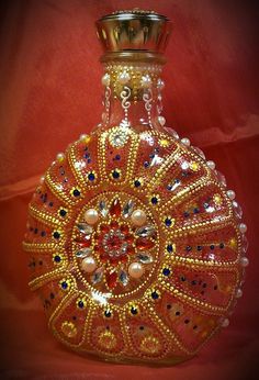 a decorative glass bottle with gold trimmings and beads on the top, sitting against a red background