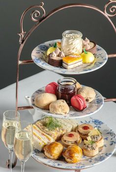 two tiered trays filled with pastries and desserts next to a glass of wine