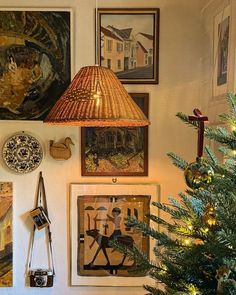 a christmas tree is in front of pictures on the wall and a lamp hanging above it