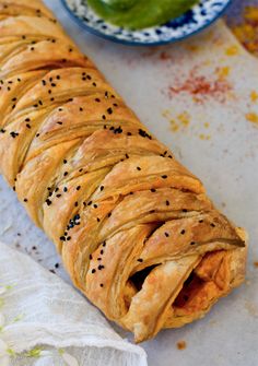 a long pastry with black seeds on it next to a bowl of pickle leaves