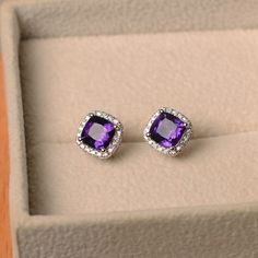 This earrings features a 6*6mm cushion cut natural amethyst and sterling silver finished with rhodium. Customization is available. It is made by hand, and it will take about 7 days to finish the ring after your payment is completed. Main stone: natural 6*6mm cushion cut amethyst Metal type: sterling silver finished with rhodium Accent stone: cz Customization is available, I also can make it with 14k solid gold (white or yellow or rose) and diamond accent stone, just feel free to contact me. Any Purple Cushion Cut Jewelry Gift, Cushion Cut Gemstone Earrings For Gift, Purple Halo Jewelry As A Gift, Amethyst Earrings Studs, Amethyst Earrings Gold, Gemstone Jewelry Earrings, Original Engagement Rings, Halo Diamond Earrings, Amethyst Studs