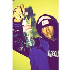 a man holding up a coke bottle in his right hand and wearing a beanie