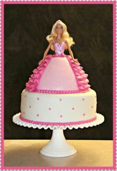 a barbie doll sitting on top of a pink and white cake