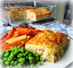 a white plate topped with green peas next to a casserole and potato dish