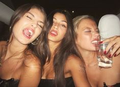 three beautiful young women sitting next to each other holding wine glasses in their hands and laughing