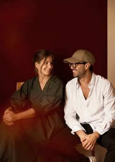 a man and woman sitting next to each other in front of a red wall smiling