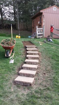 there is a wheelbarrow on the grass with steps leading up to it and a man standing in the background