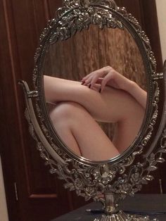 a woman's legs are visible in the reflection of an ornately decorated mirror