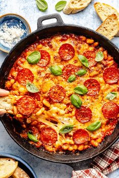 a pizza in a skillet with basil and cheese on the side next to bread