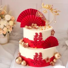 a three tiered cake with red decorations and fan decoration on top, sitting on a table