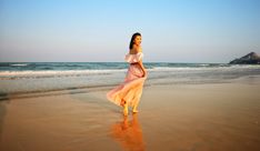 a woman is walking on the beach with her dress blowing in the wind