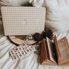 an open laptop computer sitting on top of a bed next to a book and pine cones