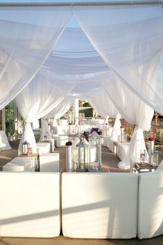 an outdoor seating area with white draping and pillows on the couches,