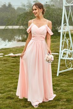 a woman in a long pink dress standing on the grass near a swing and holding a bouquet