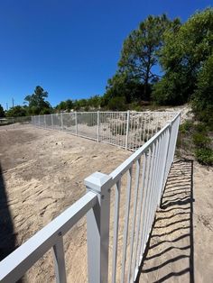 a white fence is on the side of a dirt road