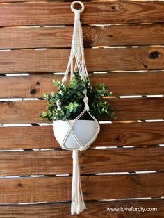 a white hanging planter with green plants in it on a wooden fence wall background