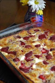 a dessert dish with strawberries and cream in it sitting on a table next to a flower vase