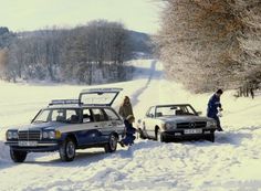 two cars parked in the snow with people looking at them