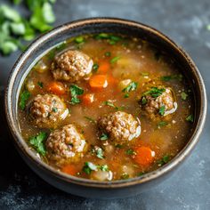 a bowl of soup with meatballs and carrots on the side next to some parsley