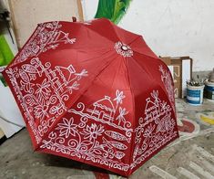 a red umbrella with white designs on it sitting in the middle of a room next to a green parrot