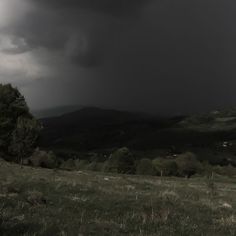 a black and white photo of a storm moving through the sky over a grassy field