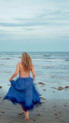 a woman in a blue dress walking on the beach with her back to the camera