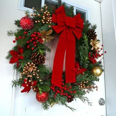 a christmas wreath on the front door with red and gold ornaments hanging from it's side