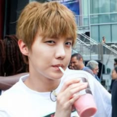 a young man drinking from a pink cup while standing in front of a group of people