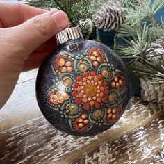 a hand holding an ornament in front of pine cones