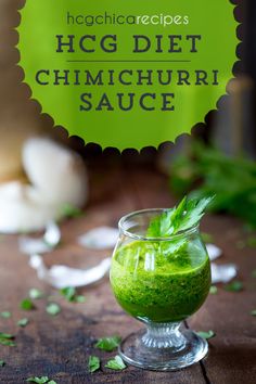 a glass filled with green liquid on top of a wooden table next to garlic and herbs