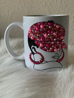 a white coffee mug with pink and black beads on it's face, sitting on a fur surface