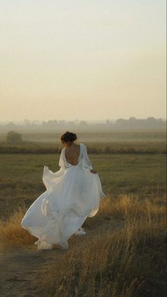 a woman in a white dress walking across a field