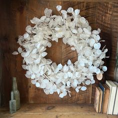 a wreath with white flowers on top of a book shelf next to an open book