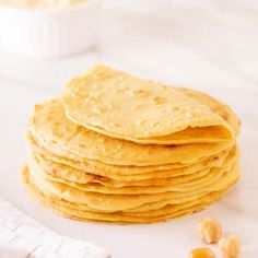 a stack of corn tortillas sitting on top of a white tablecloth next to a bowl of chickpeas