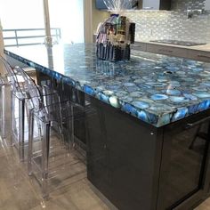 a kitchen island with blue marble countertops and clear acrylic chairs around it