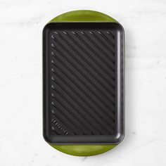 an empty black tray sitting on top of a white counter next to a green plate