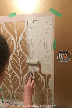 a woman is painting a wall with brown and white stencils in the process of remodeling