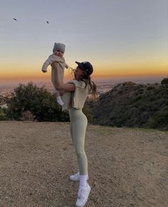 a woman holding a baby in her arms on top of a dirt hill at sunset