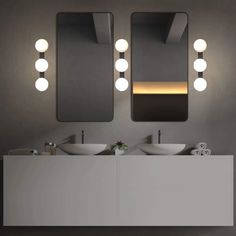 two sinks and mirrors in a bathroom with lights on the wall above them that are dimming