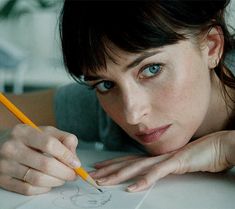 a woman is laying down with her hand on the paper and holding a pencil in front of her face