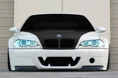 the front end of a white bmw car with its hood up and headlight on